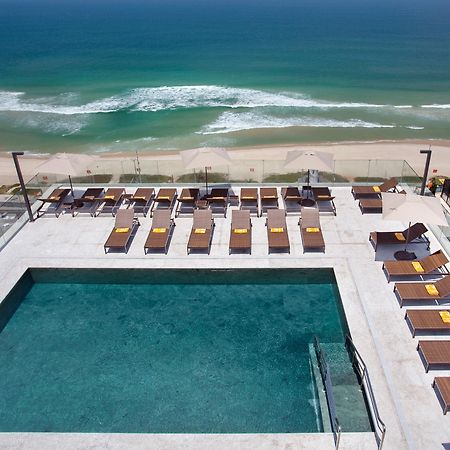 ホテル ウィンザー マラペンディ リオデジャネイロ エクステリア 写真 The photo shows a rooftop area with a swimming pool and several lounge chairs arranged around it. The pool has a clear blue surface, and the lounge chairs are positioned in a neat row, some with yellow cushions. In the background, you can see a beaut