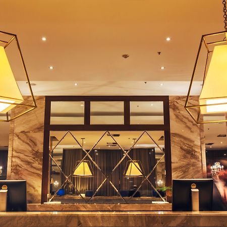 ホテル ウィンザー マラペンディ リオデジャネイロ エクステリア 写真 The photo shows a hotel lobby or reception area. There are large geometric light fixtures hanging from the ceiling, providing a warm glow to the space. The reception desk is made of a polished material, likely marble, with decorative elements and two