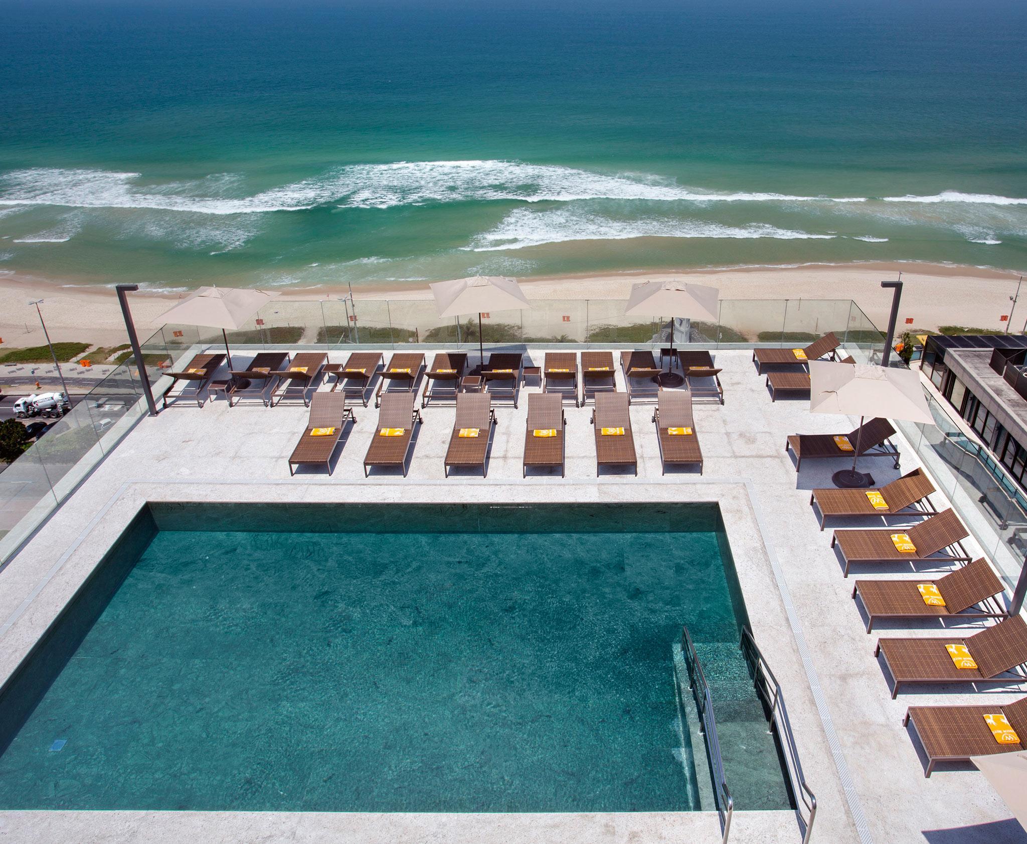 ホテル ウィンザー マラペンディ リオデジャネイロ エクステリア 写真 The photo shows a rooftop area with a swimming pool and several lounge chairs arranged around it. The pool has a clear blue surface, and the lounge chairs are positioned in a neat row, some with yellow cushions. In the background, you can see a beaut